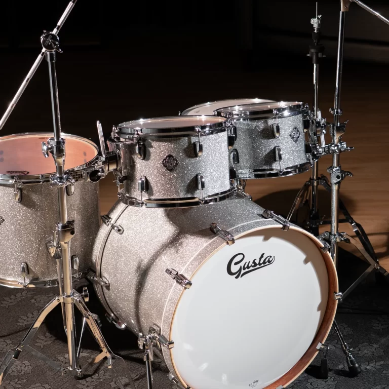 Shiny silver glitter drum kit with bass drum labeled 'Gusta' set up on a dark stage. ขายราคาพิเศษ