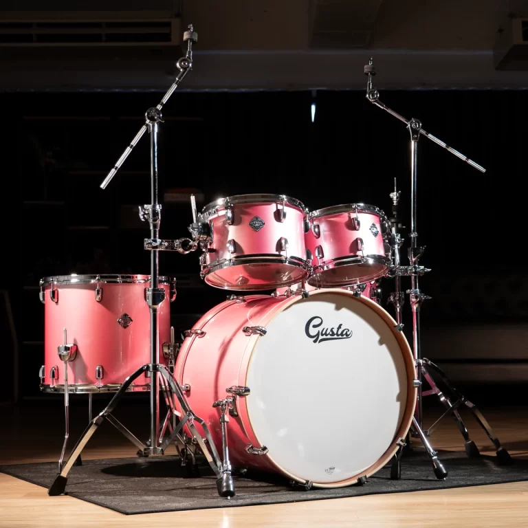 Pink drum kit on a stage with chrome hardware and a white bass drum head that reads 'Gusta'. ขายราคาพิเศษ