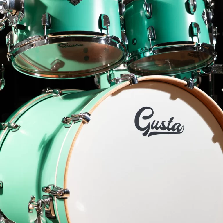 Close-up of a mint-green drum set with chrome hardware and a white bass drum head that reads 'Gusta' in script. ขายราคาพิเศษ
