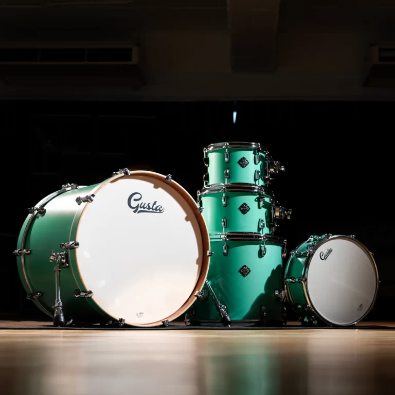 Teal drum kit on a dim stage, large bass drum with 'Gusta' logo, and stacked toms in the center. ขายราคาพิเศษ