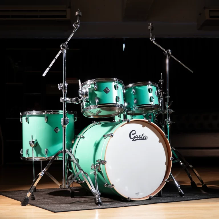 Emerald-green drum kit on a wooden stage with a white bass drum head reading 'Gusta' and chrome hardware. ขายราคาพิเศษ