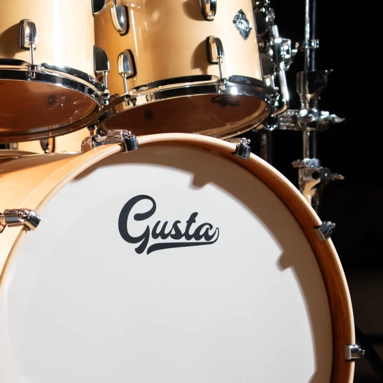 Close-up of a beige drum set with chrome hardware, featuring a bass drum head that reads 'Gusta'. ขายราคาพิเศษ