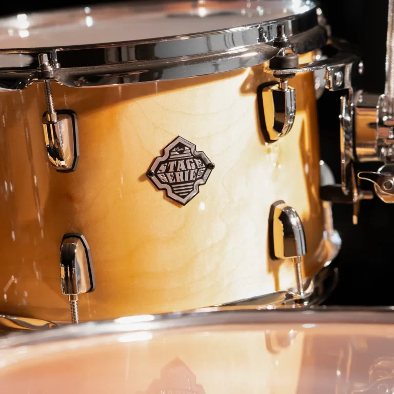 Close-up of a natural wood drum with chrome hardware and a 'Stage Series' badge on the shell, highlighting its finish and lugs. ขายราคาพิเศษ