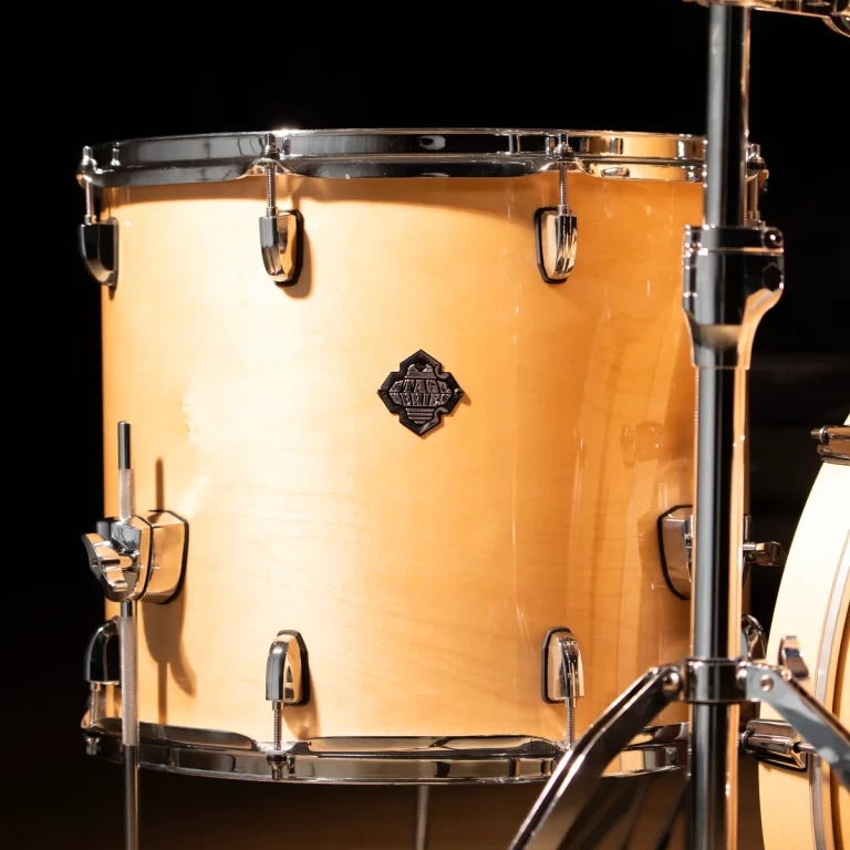 Close-up of a light wood snare drum with chrome hoops and lugs, mounted on a stand against a dark background. ขายราคาพิเศษ