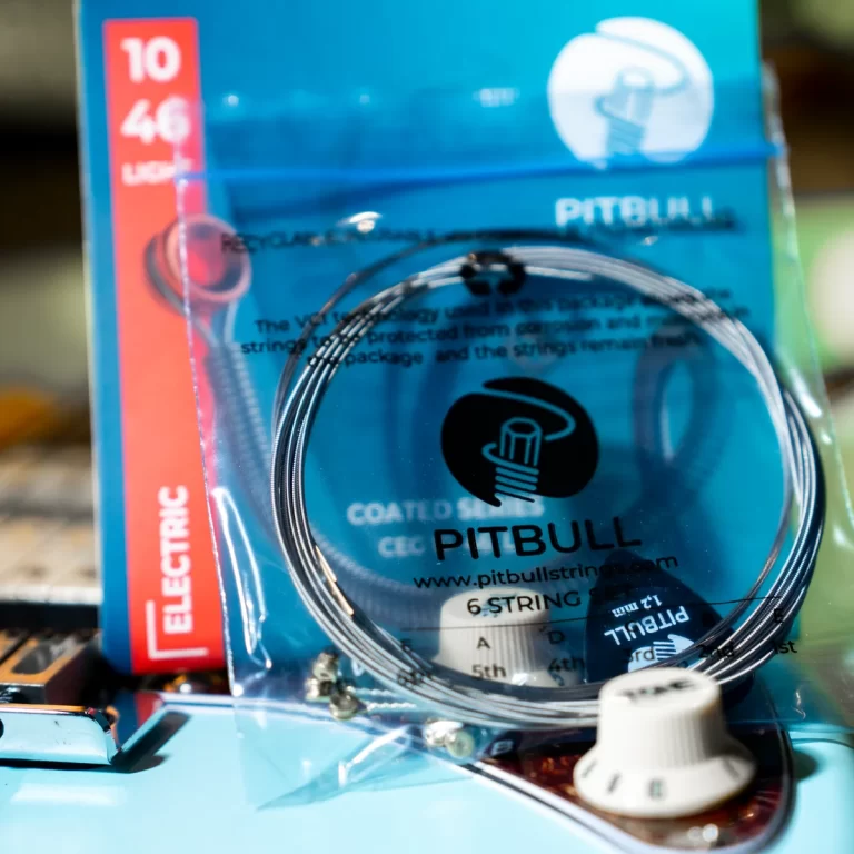 Package of Pitbull brand six-string guitar strings in blue packaging with a coiled string visible on a turquoise guitar body. ขายราคาพิเศษ