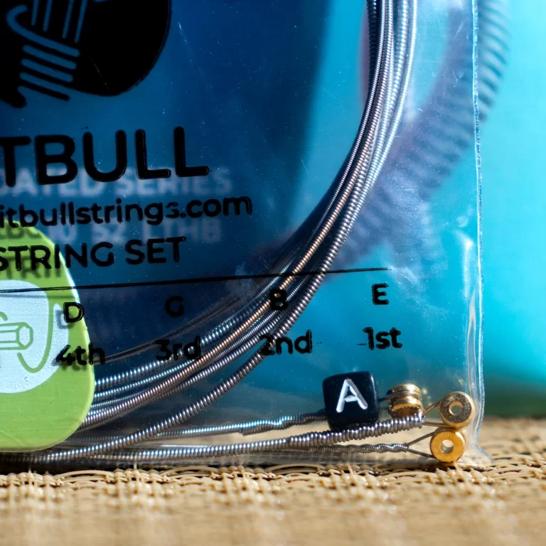 Close-up of a blue-packaged guitar string set with coiled metal strings and a small black keycap labeled A resting on the strings. ขายราคาพิเศษ