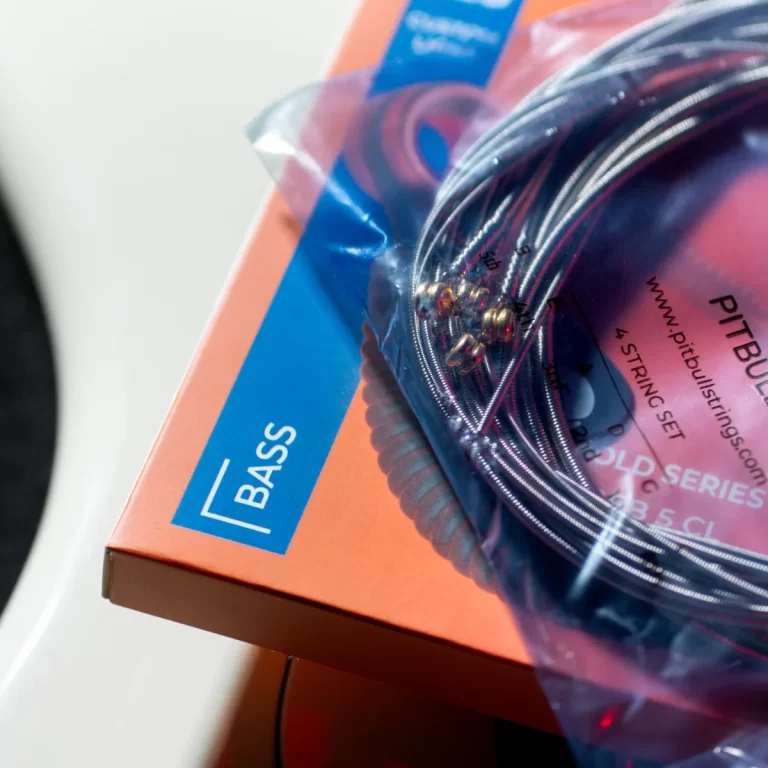 Coiled bass guitar strings in a clear plastic bag resting on an orange retail box labeled BASS. ขายราคาพิเศษ
