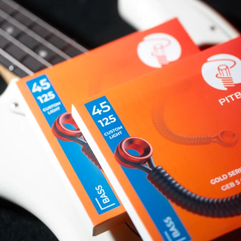 Close-up of orange guitar string boxes labeled 45 125 and Custom Light, resting on a white guitar body. ขายราคาพิเศษ