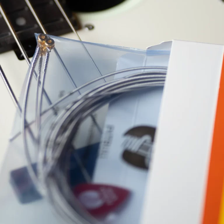 Close-up of coiled guitar strings inside a plastic bag with a blurred guitar neck in the background. ขายราคาพิเศษ