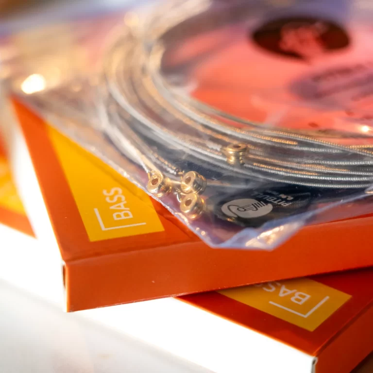 Close-up of a coiled braided audio cable in a clear plastic bag resting on orange packaging labeled 'BASS'. ขายราคาพิเศษ