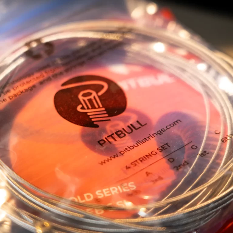 Close-up of a Pitbull Strings guitar string set packaging with an orange label inside a clear plastic case. ขายราคาพิเศษ