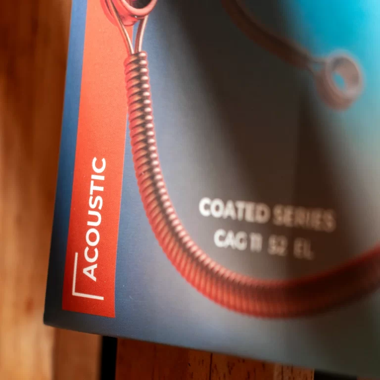 Close-up of a product package showing a red vertical label reading 'ACOUSTIC' and a coiled copper cable, with blurred white text 'COATED SERIES' and 'CAG II 52 IH' in the background. ขายราคาพิเศษ
