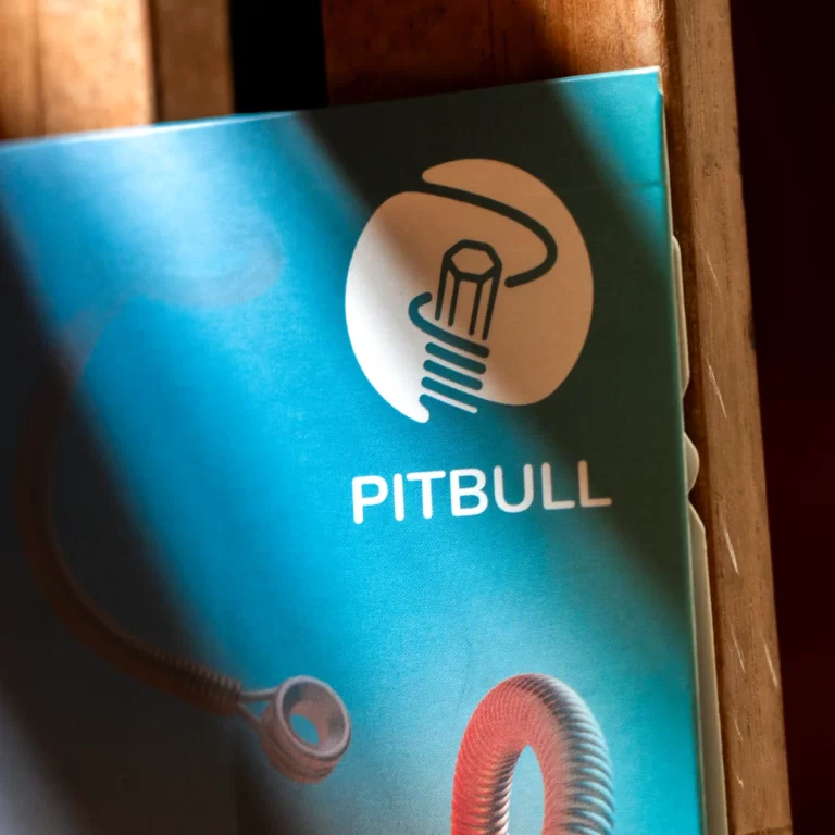 Blue product packaging with a white circular lightbulb logo and the word PITBULL on a turquoise background. A coiled cord is visible at the bottom left. ขายราคาพิเศษ