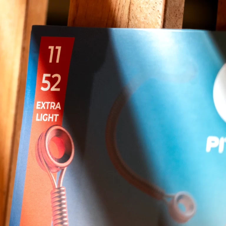 Close-up of a blue product package with a vertical red label reading '11 52 EXTRA LIGHT' and a red circular component nearby. ขายราคาพิเศษ