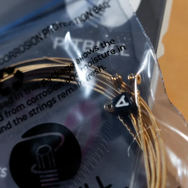 Close-up of a gold braided wire coil inside a clear plastic bag, with a small black component labeled with a white symbol nearby and protective text visible on the bag edge. ขายราคาพิเศษ