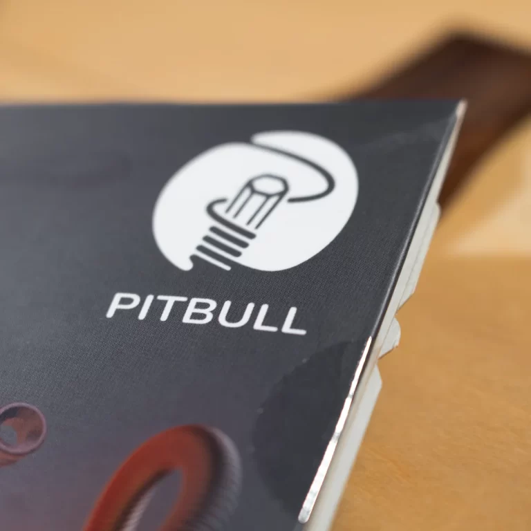 Close-up of a dark notebook cover with a white circular logo and the word PITBULL printed on it. ขายราคาพิเศษ