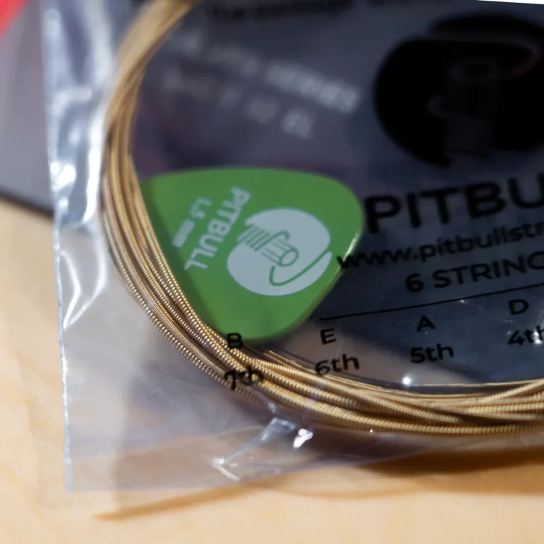 Green guitar pick resting on a stack of gold guitar strings in a clear bag.Typical guitar accessory kit content. ขายราคาพิเศษ