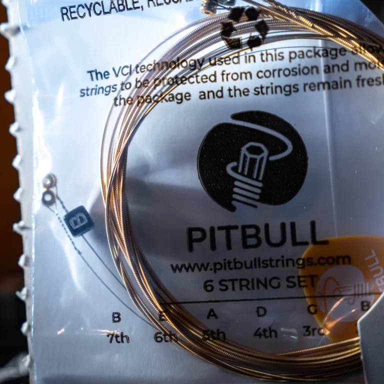 Close-up of a Pitbull guitar strings package showing a six-string set, coiled bronze-wound strings, and the Pitbull logo with the URL www.pitbullstrings.com. ขายราคาพิเศษ