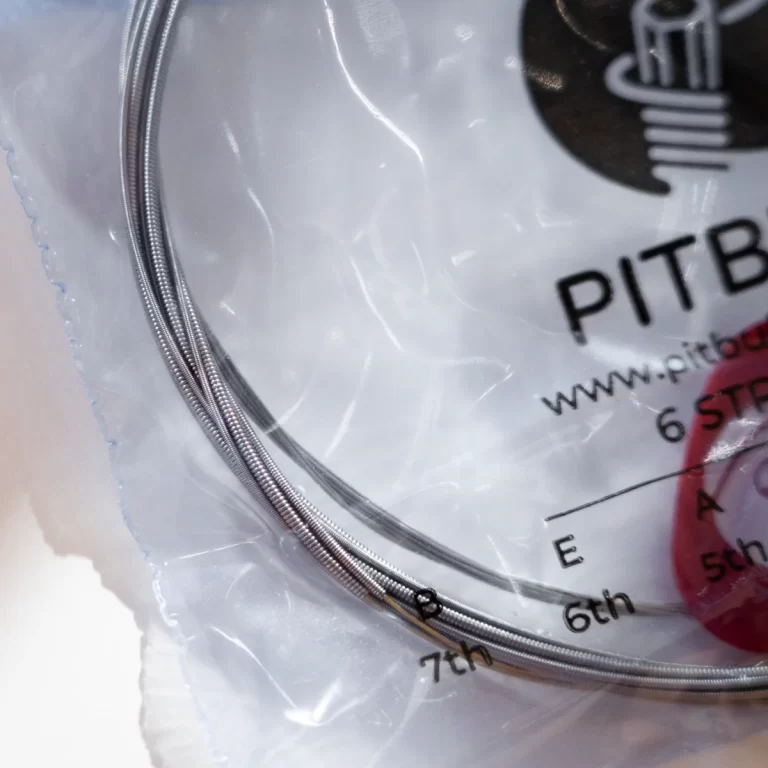 Close-up of a coiled stainless steel wire rope inside a clear plastic bag with printed text and logos visible behind it. ขายราคาพิเศษ