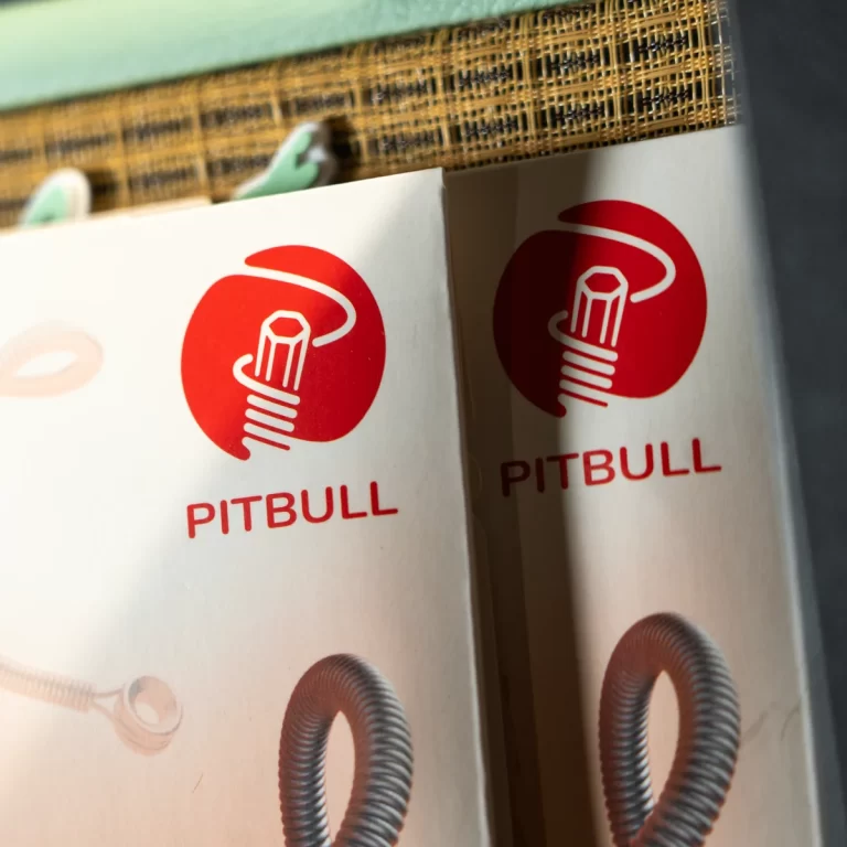 Two white packaging boxes side by side showing a red circular Pitbull logo and the word 'PITBULL' beneath it on a shelf surface. ขายราคาพิเศษ