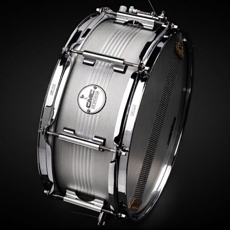 Shiny metal snare drum photographed against a dark background, showing lugs and hoops clearly centered on the shell. ขายราคาพิเศษ