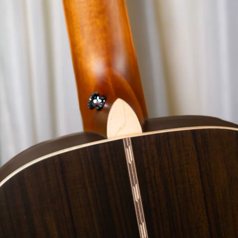 Close-up of the back of a dark wood acoustic guitar with a lighter neck heel and a decorative inlay along the seam. ขายราคาพิเศษ