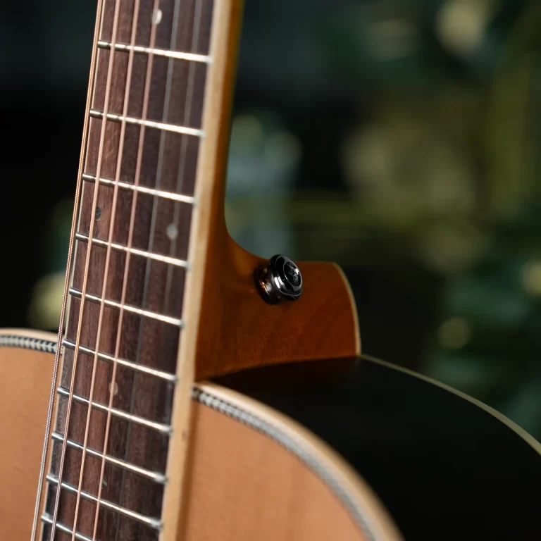 Close-up of a wooden acoustic guitar neck and body with a black strap button mounted on the side near the cutaway. ขายราคาพิเศษ