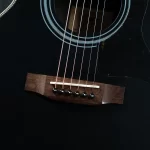 Close-up of a black acoustic guitar showing the bridge, saddle, and six strings anchored to the bridge. The glossy body and soundhole rings are visible. ขายราคาพิเศษ