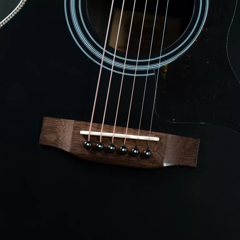 Close-up of a black acoustic guitar showing the bridge, saddle, and six strings anchored to the bridge. The glossy body and soundhole rings are visible. ขายราคาพิเศษ