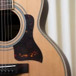 Close-up of an acoustic guitar body showing the sound hole, rosette, tortoiseshell pickguard, and decorative binding along the edge. ขายราคาพิเศษ