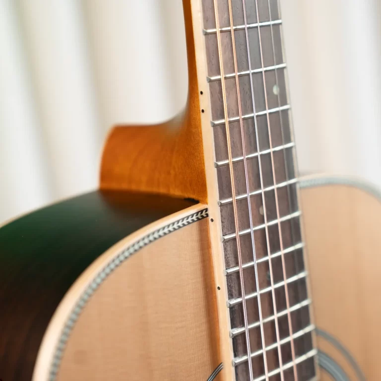 Close-up of a wooden acoustic guitar neck with frets and six strings, showing the soundboard edge and binding ขายราคาพิเศษ