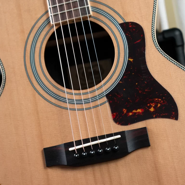 Close-up of an acoustic guitar showing the soundhole, six strings, and tortoiseshell pickguard on a wooden body. ขายราคาพิเศษ