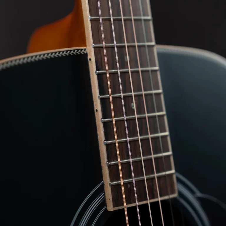 Close-up of an acoustic guitar neck with wooden fretboard, metal frets, and six strings against a dark background ขายราคาพิเศษ