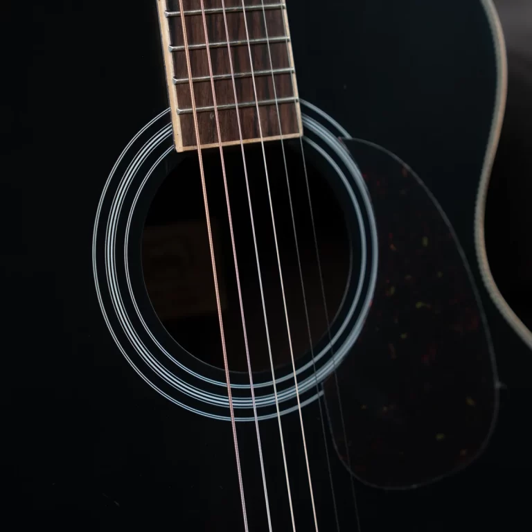 Close-up of a black acoustic guitar showing the sound hole and multiple steel strings across the fretboard area. ขายราคาพิเศษ