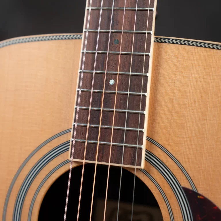 Close-up of an acoustic guitar neck with six strings over the dark fretboard and soundhole visible at the bottom ขายราคาพิเศษ