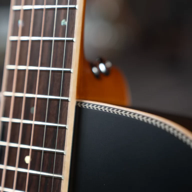 Close-up of an acoustic guitar neck showing frets and strings, with the body blurred in the background ขายราคาพิเศษ