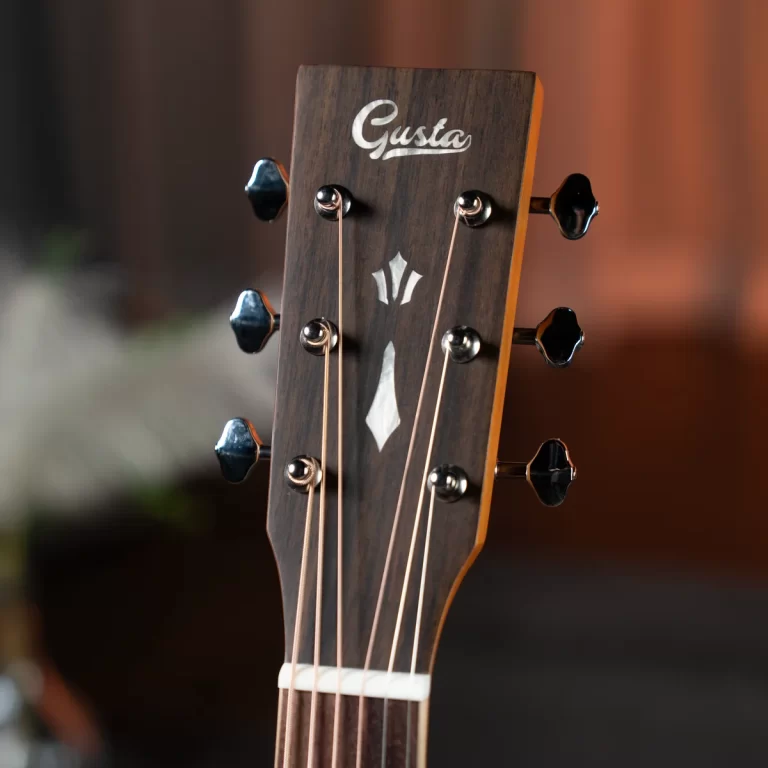Close-up of a guitar headstock with six tuning pegs on dark wood and the brand 'Gusta' visible on the headstock accessory plate. ขายราคาพิเศษ