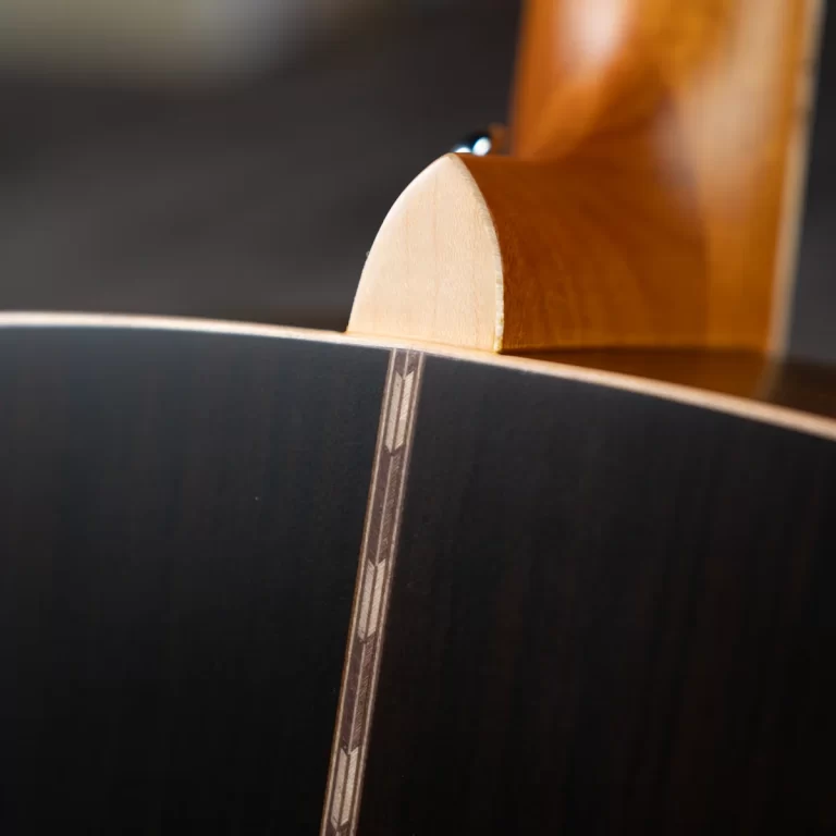 Close-up of a guitar neck heel joining the body, showing wood grain and dark back with decorative binding along the edge. ขายราคาพิเศษ