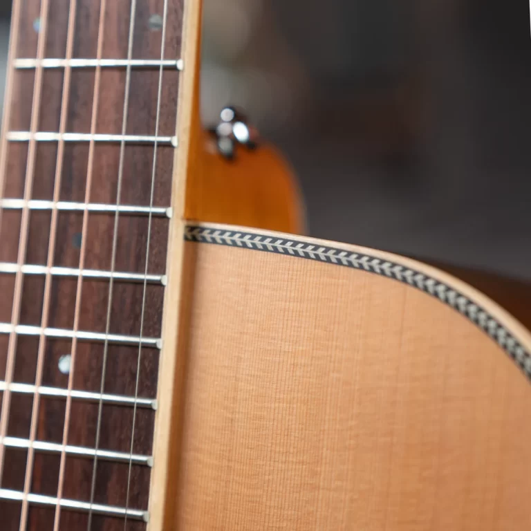 Close-up of an acoustic guitar neck and body: fretboard with metal frets and strings on the left, and the curved wooden body with a black-and-white braided strap edge on the right. ขายราคาพิเศษ