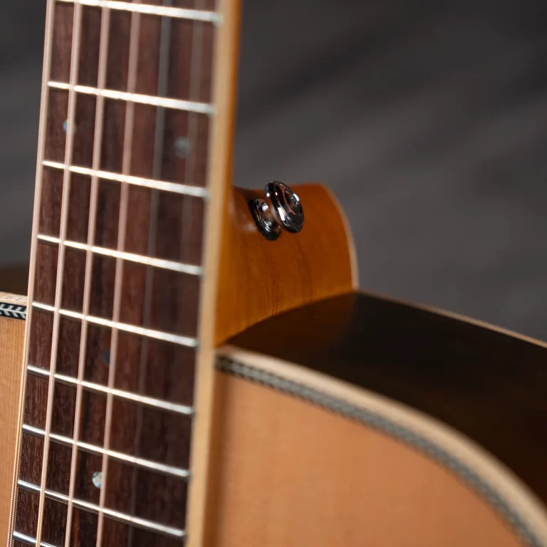 Close-up of an acoustic guitar neck and body, showing the fretboard, strings, and a mounted strap button on the side. ขายราคาพิเศษ