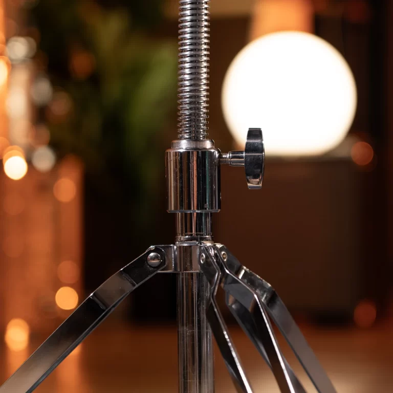 Close-up of a chrome adjustable tripod stand with a threaded central column and locking knob in a warm studio setting. ขายราคาพิเศษ
