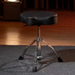 Black padded drum throne with a chrome tripod base on a stage floor ลดราคาพิเศษ