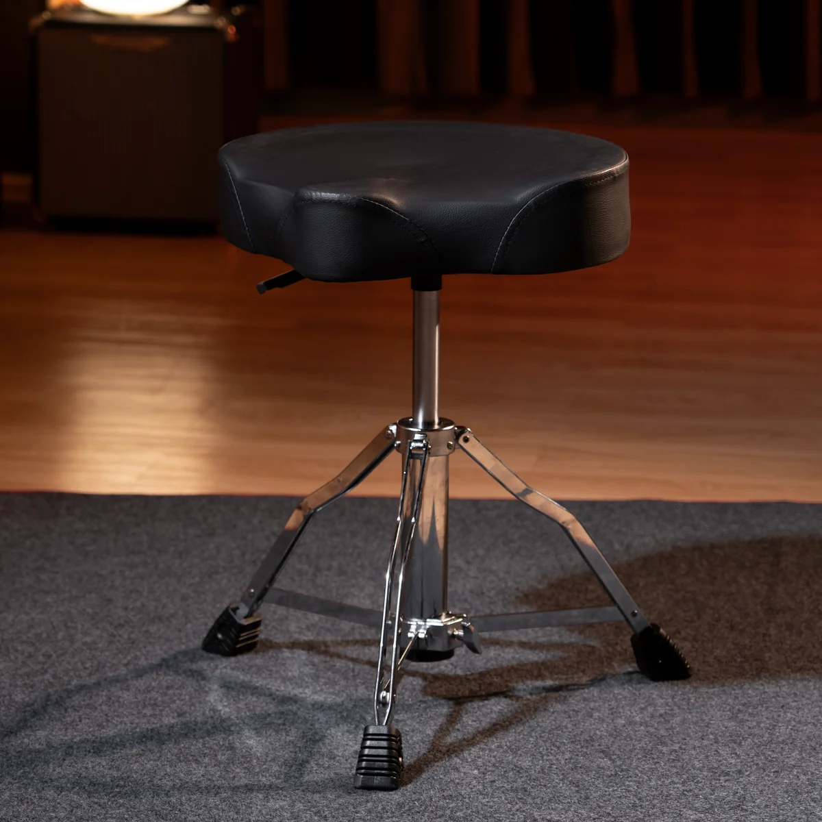 Black padded drum throne with a chrome tripod base on a stage floor