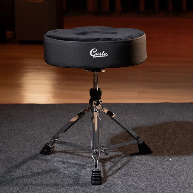 Round black padded drum throne with a three-leg chrome base on a stage-floor, adjustable height for drummers (brand: Gusta). ขายราคาพิเศษ