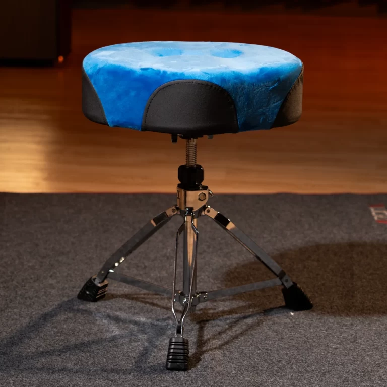 Round blue cushioned drum throne with a black base, on a three-legged chrome stand on a carpeted stage floor. ขายราคาพิเศษ
