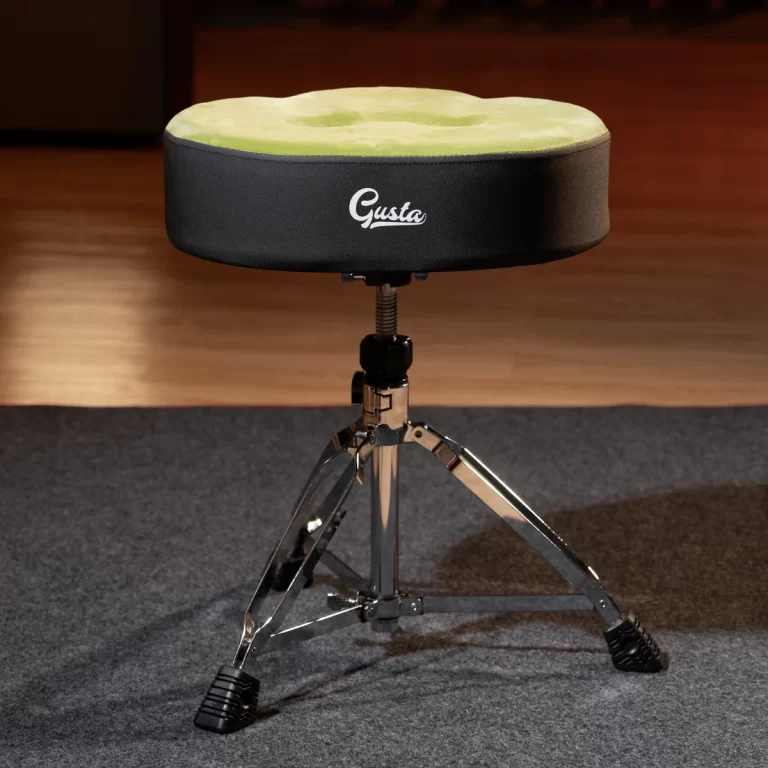 Drum throne with a lime green padded top and a three‑leg chrome base on a carpeted studio floorStorming stand and height adjustment visible, Gusta logo on the cover ขายราคาพิเศษ