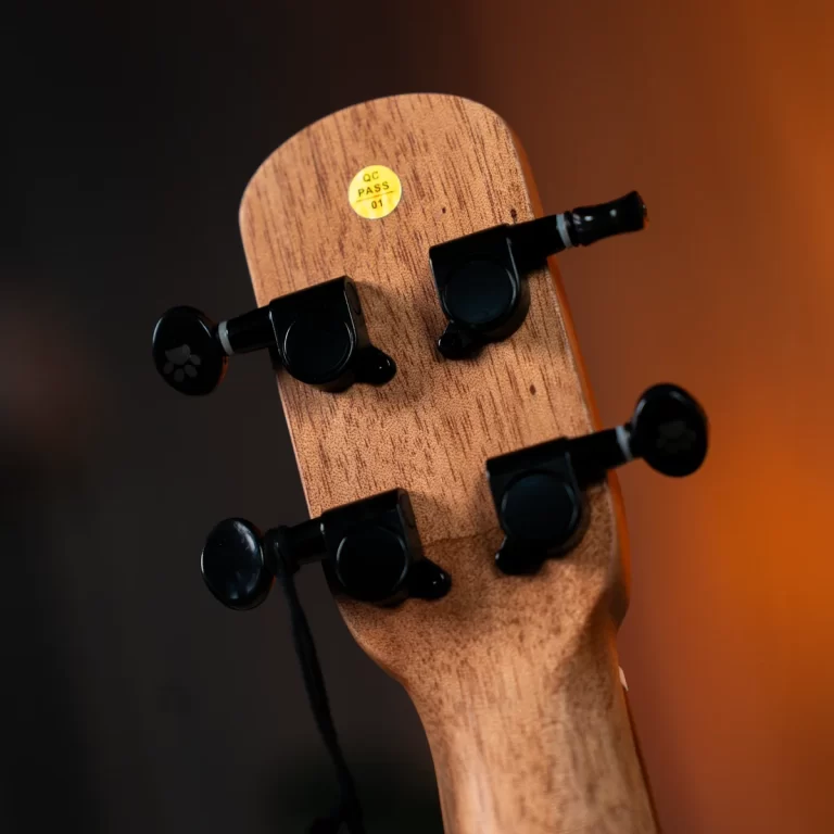 Close-up of a wooden guitar headstock with black tuning pegs and a yellow QC Pass sticker in the center ขายราคาพิเศษ