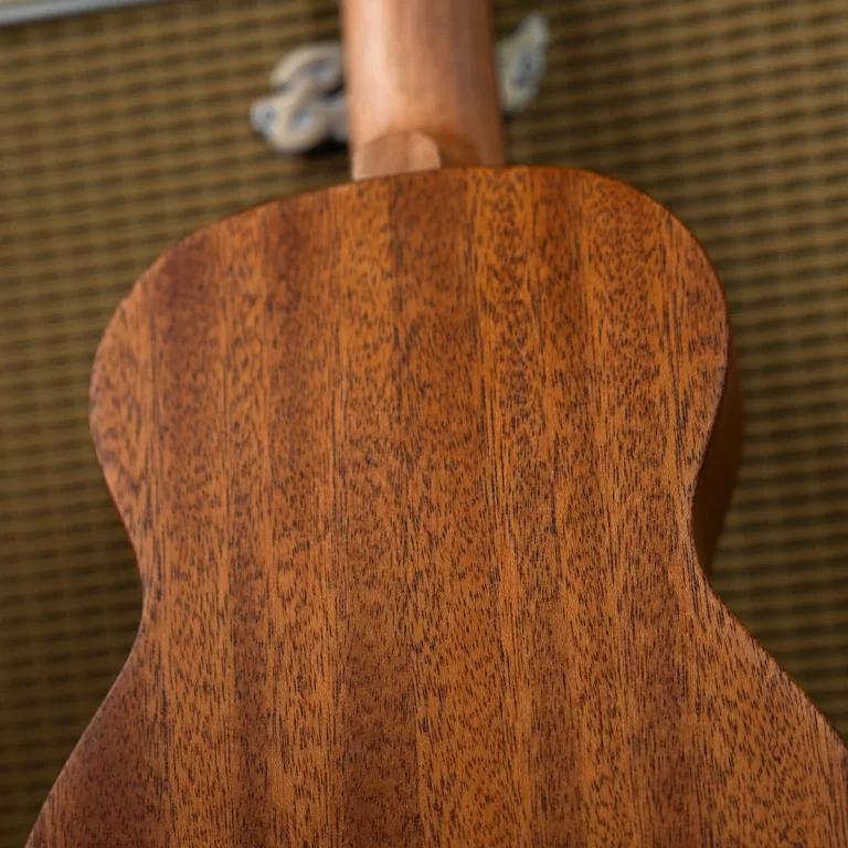 Close-up of a wooden guitar back with a rich brown grain pattern, neck at the top and tuning pegs visible in the blurred background. ขายราคาพิเศษ