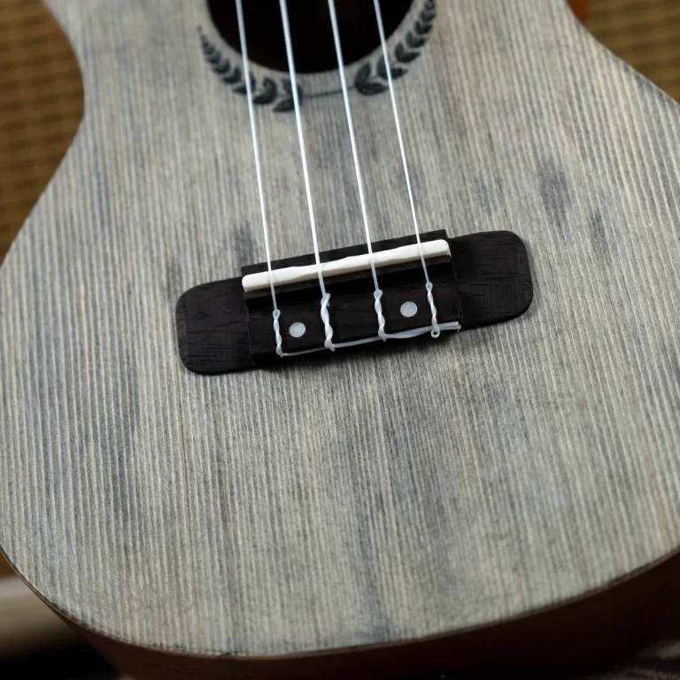 Close-up of an acoustic guitar bridge with four strings on a light, textured wooden body ขายราคาพิเศษ