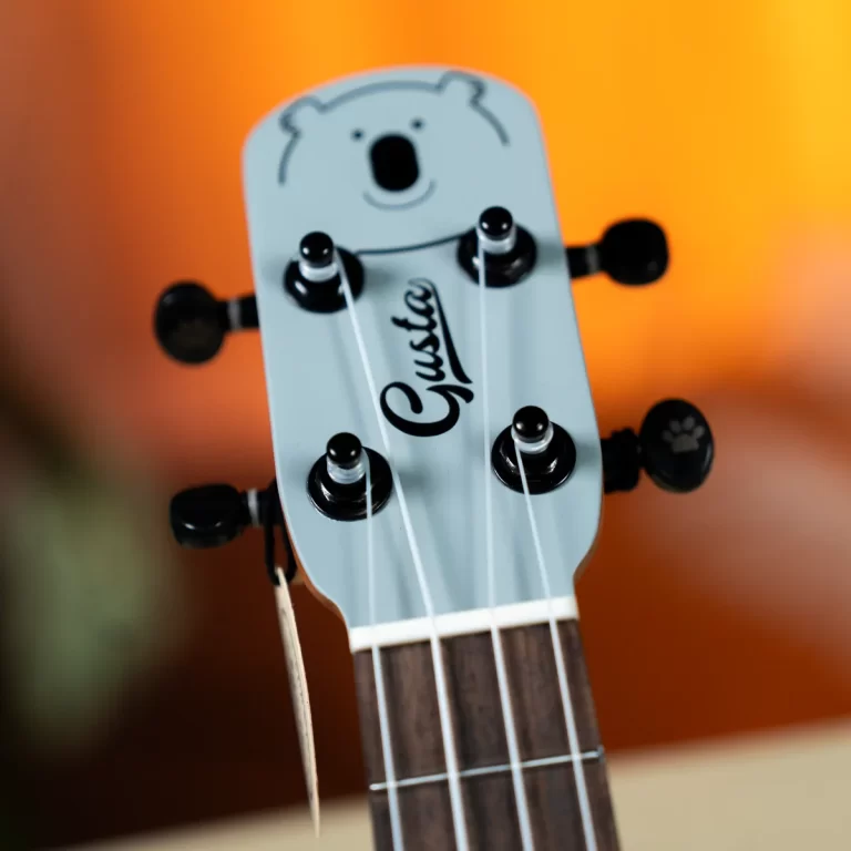 Close-up of a light-blue guitar headstock with six tuning pegs and white strings against a warm orange blurred background. ขายราคาพิเศษ